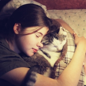 A girl and her cat sleeping together in bed